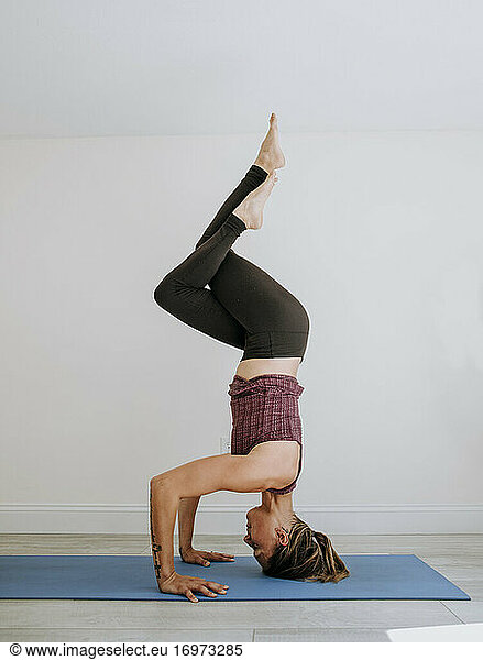 Fit athletic muscular woman does headstand yoga pose indoors