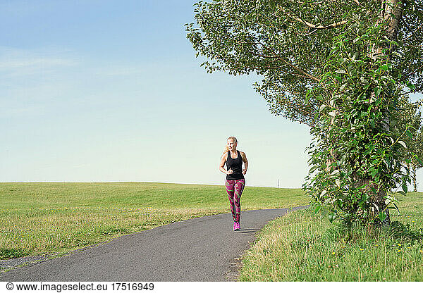 Fit blondie running on path in countryside against cloudless blue sky