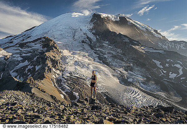 Fit female standing on a cliff next to Mount Rainier smiling at camera
