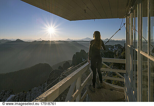 Fit female with leggings standing on deck of fire lookout at sunrise