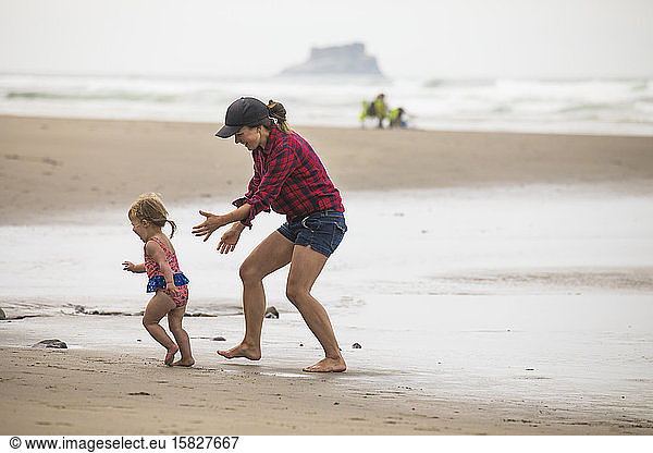 fit  fun mother playfully chases her young daughter on the beach.