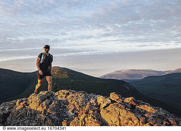 fit male hiker walks along rocky trail at sunrise in Maine mountains