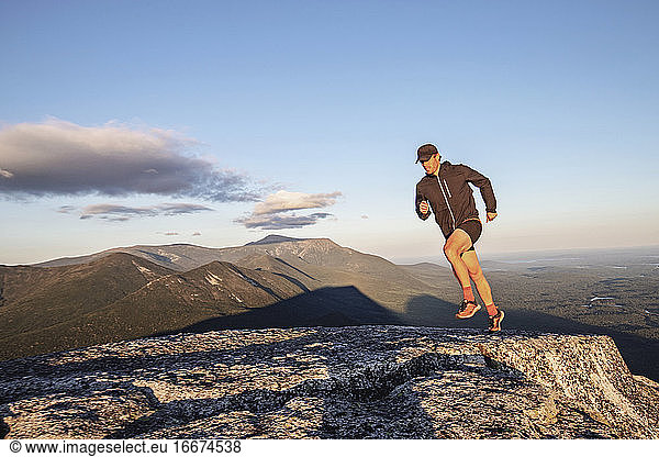 fit male trail runner runs across rocks on summit of Doubletop  Maine