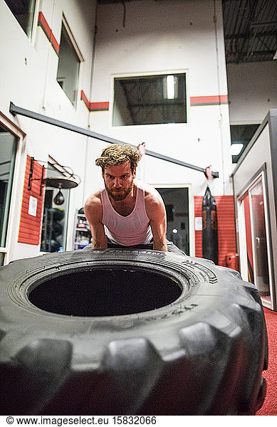 Fit man lifting large tire in gym
