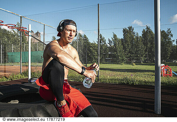 Fit man with water bottle sitting on tire at park