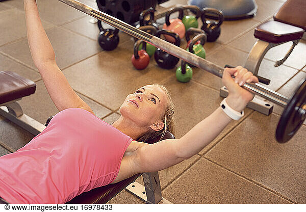 Fit woman exercising with barbell on bench
