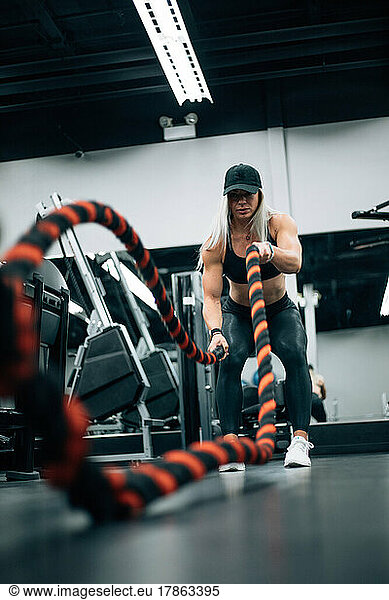 Fit woman with blonde hair doing rope workout in gym