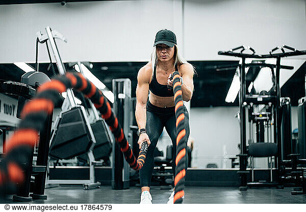 Fit woman with blonde hair doing rope workout in gym