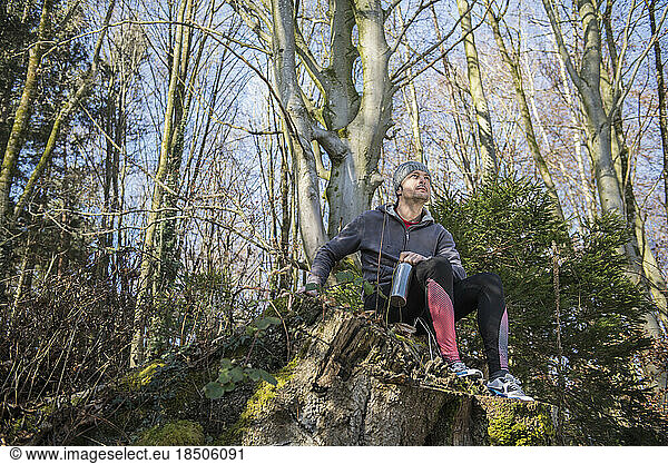 Fit young man relaxing on tree stump in forest