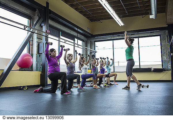 Fitnesstrainerin  die Frauen beim Hantelnheben im Fitnessstudio anleitet