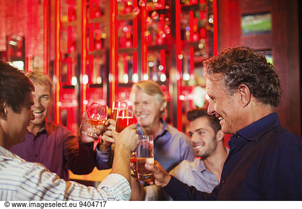 Five smiling men raising toast in bar
