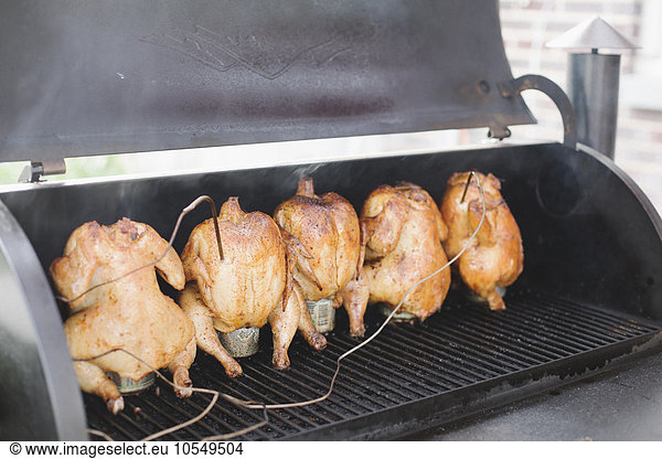 Five whole chickens roasting on a barbecue.