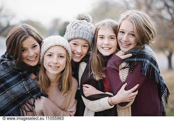 Five young people girls friends in warm shawls and woolly hats outdoors.