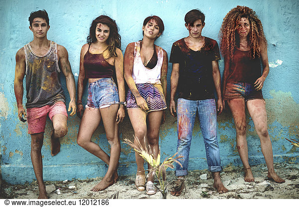 Five young people lined up against a wall covered in paint looking at camera.