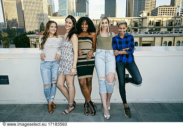 Five young women posing for photographs on a rooftop  city skyline background
