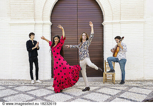 Flamenco dancers performing with guitarist in front of door