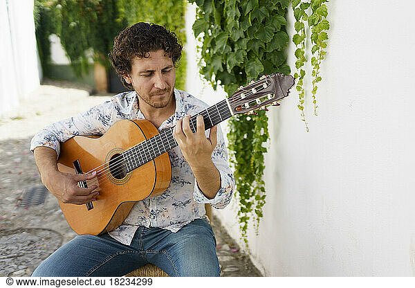 Flamenco guitarist performing by white wall with ivy plants