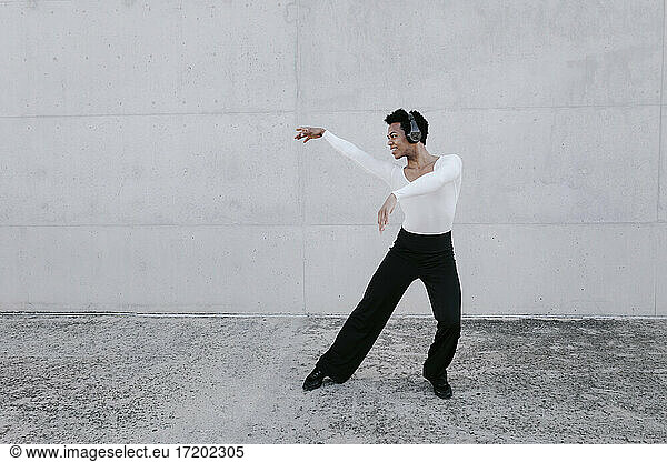Flexible man wearing headphones dancing against white wall