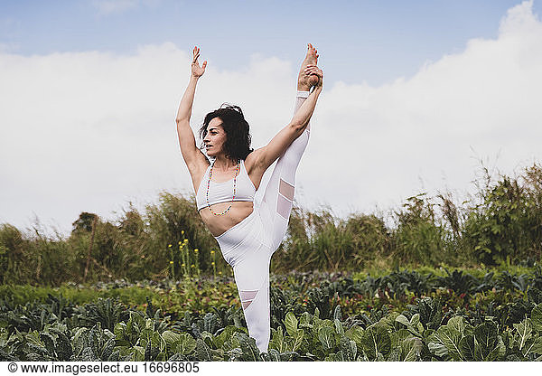Flexible woman practices yoga in a field