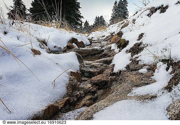 Fließendes Flusswasser in der Nähe der verschneiten Straße im Winter zur Neujahrszeit.