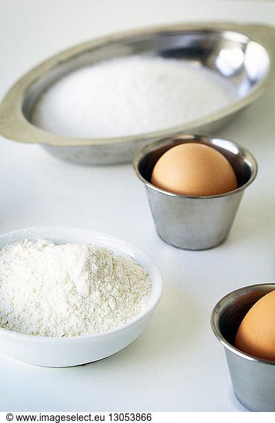 Flour and eggs in containers on table