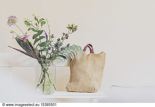 Flower vase and open calendar on white bench, linen shopping bag