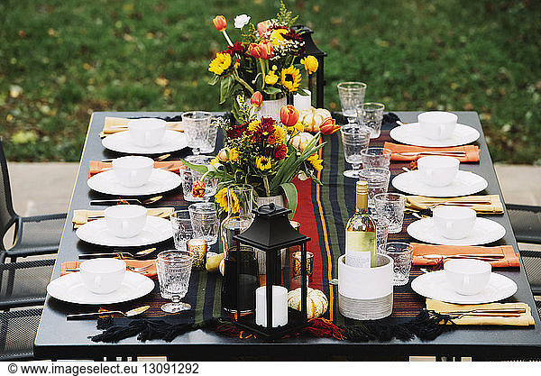 Flower vases with crockery arranged on dining table in backyard