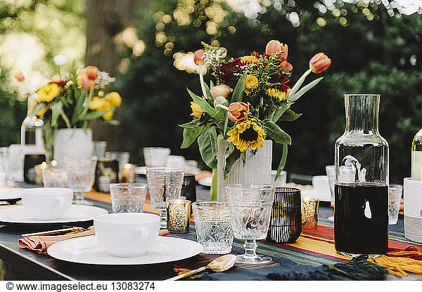 Flower vases with drinks and crockery arranged on table in backyard