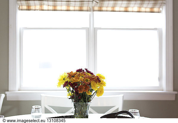 Flowers in vase against window on table at home