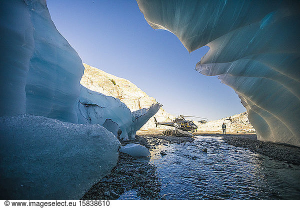 Fluss fliesst vom Gletscher in Richtung eines geparkten Hubschraubers