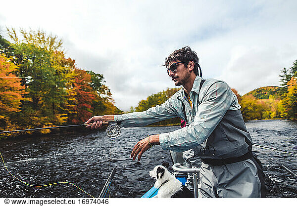 Fly fisherman casting from boat in river during fall foliage season