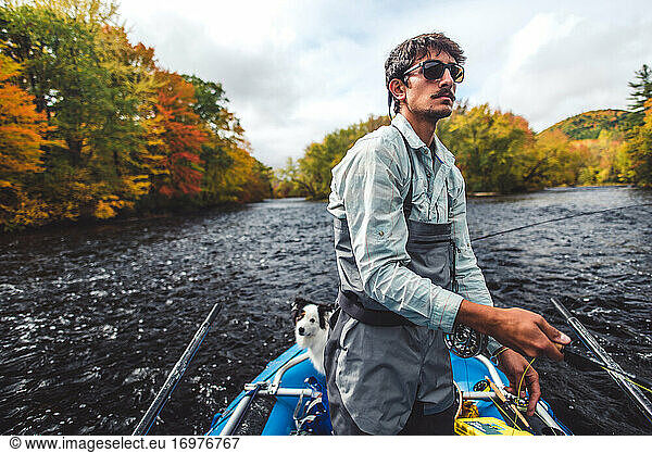 Fly fisherman casting from boat in river during fall foliage season