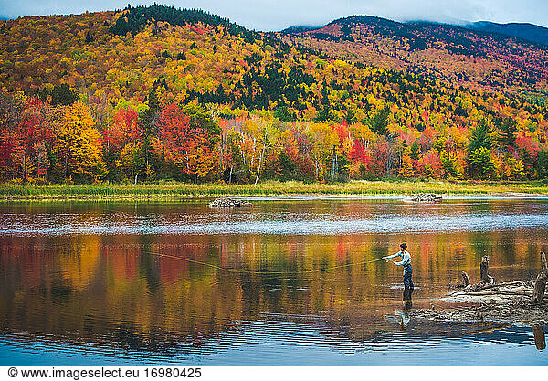 Fly fisherman casting into river with bright foliage and mountains