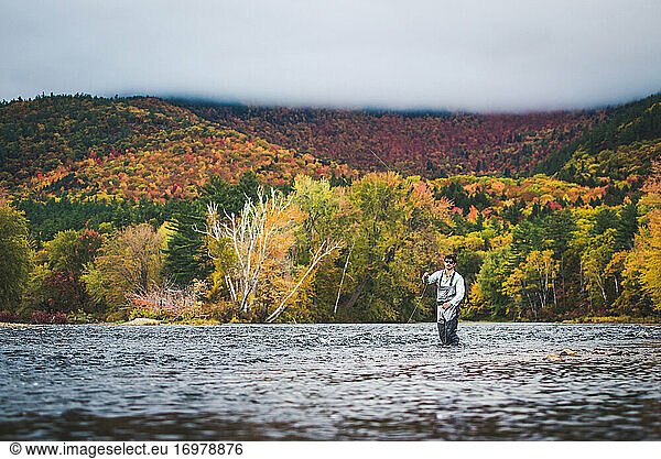 Fly fisherman casting into river with clouds and bright foliage