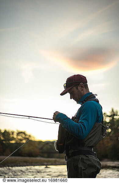 Fly-fisherman tying new fly onto his line with sunset in background