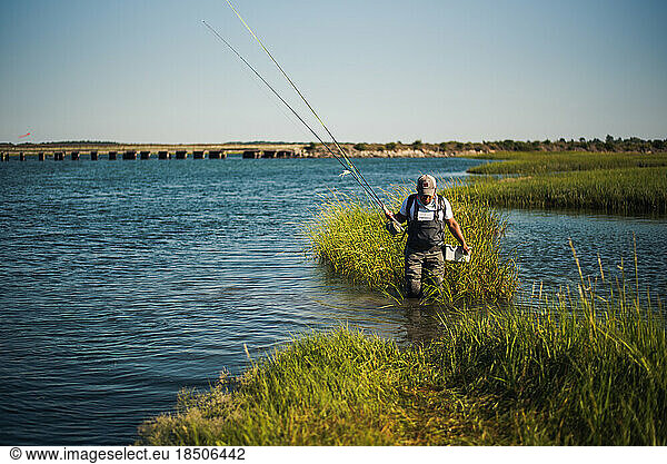 Fly fisherman wading through ocean water with sea grass