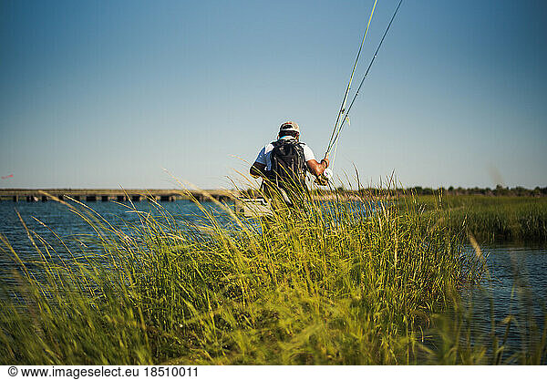 Fly fisherman wading through ocean water with sea grass
