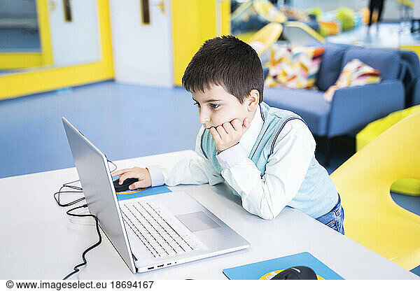 Focused boy using laptop at desk in computer class