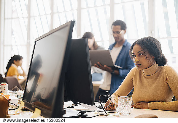 Focused businesswoman using computer while coworkers working in background at office