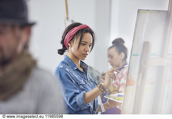 Focused female artist painting at easel in art class studio