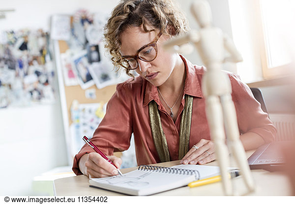 Focused female design professional sketching in notebook in office