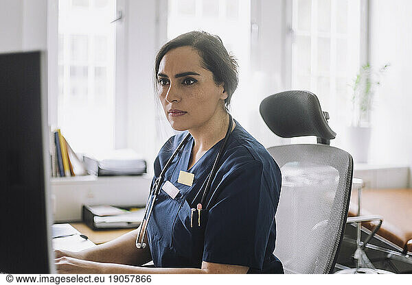 Focused female nurse working while sitting on chair in clinic