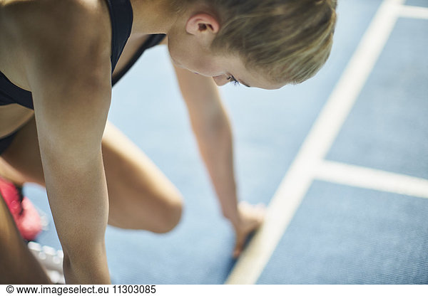 Focused female runner ready at starting block on sports track