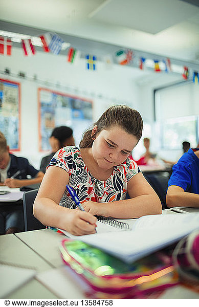 Focused junior high school girl student doing homework at desk in classroom