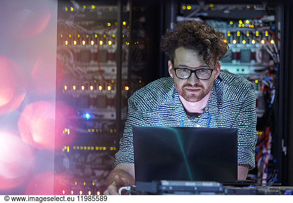 Focused male IT technician working at laptop in dark server room