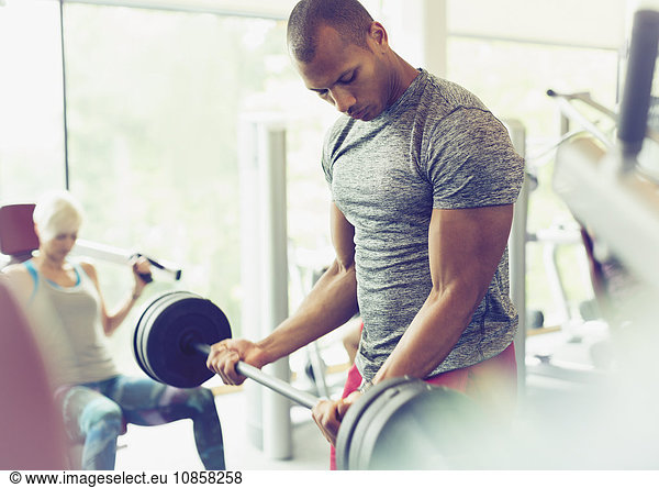 Focused man doing barbell biceps curls at gym