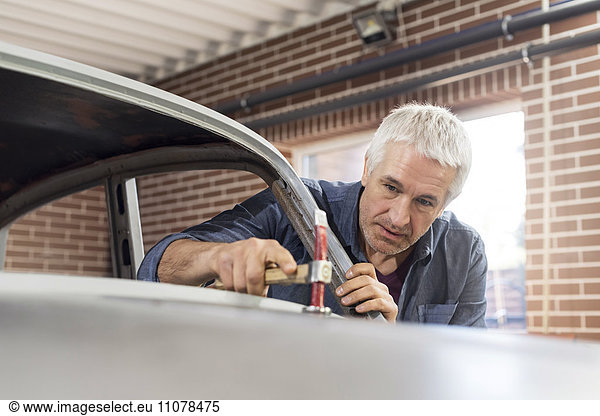 Focused mechanic using hammer on automobile hood in auto repair shop