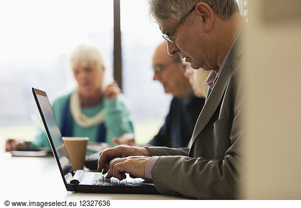 Focused senior businessman using laptop in conference room meeting