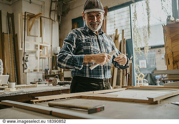 Focused senior male carpenter holding measuring tape at workshop