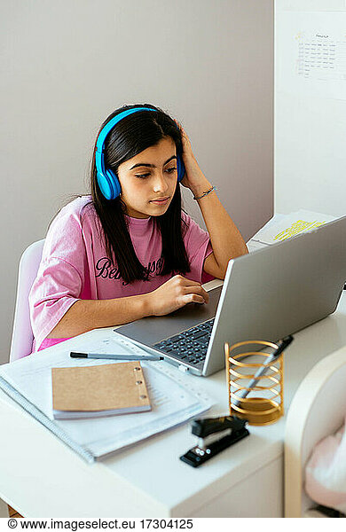 Focused teen studying at desktop listening to music in personal room